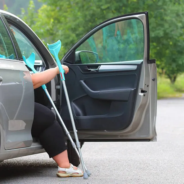 Frau mit Krücken steigt aus dem Auto aus