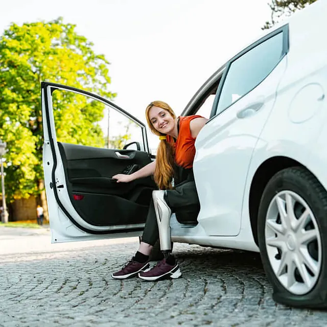 Frau mit Beinprotese steigt aus dem Auto aus
