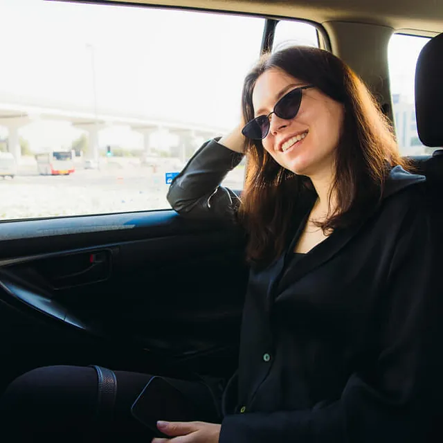 Lächelnde Frau mit Sonnenbrille sitzt im Taxi